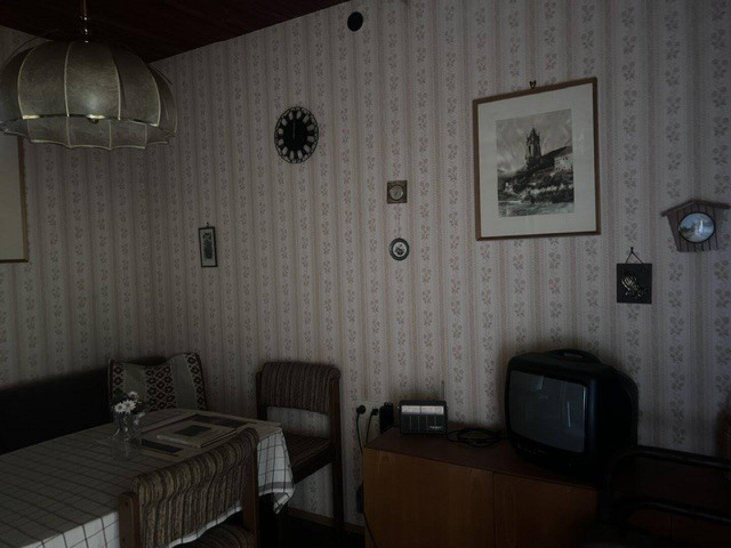Gemütlicher Essbereich mit rustikalen Möbeln, gemusterter Tapete und einem älteren Fernseher.