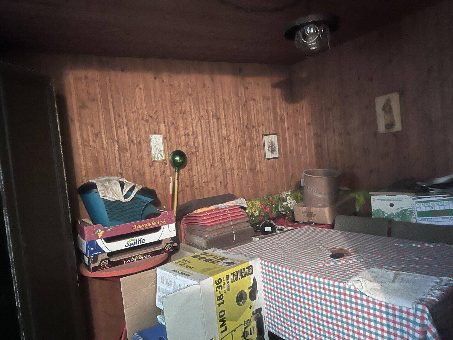 Abstellraum oder Hobbyraum mit holzvertäfelten Wänden und Decke, gefüllt mit verschiedenen Gegenständen.