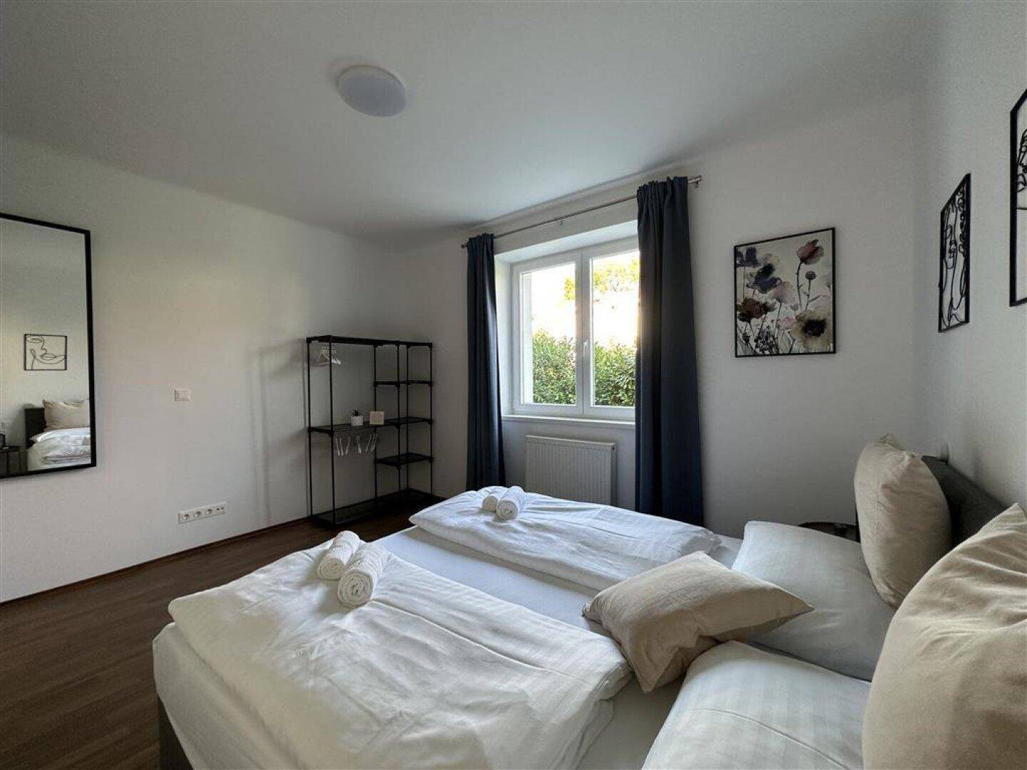 Schlafzimmer mit Doppelbett, großem Spiegel und Fenster, das viel Tageslicht hereinlässt.