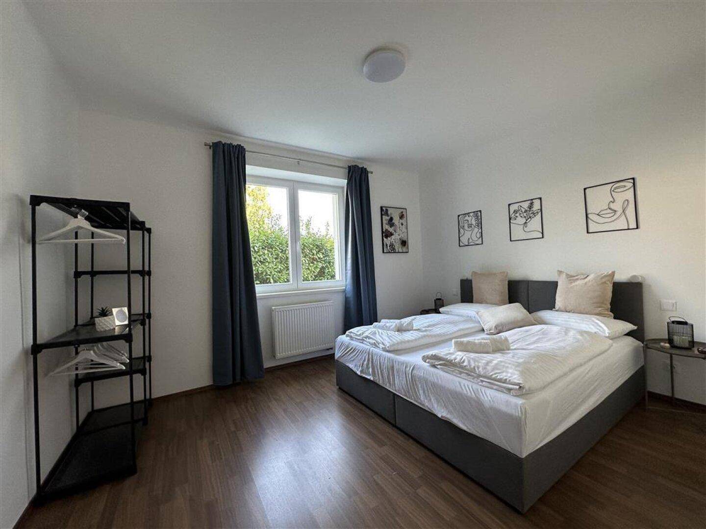 Schlafzimmer mit Doppelbett, Holzfußboden und Fenster mit Blick ins Grüne, modern eingerichtet.