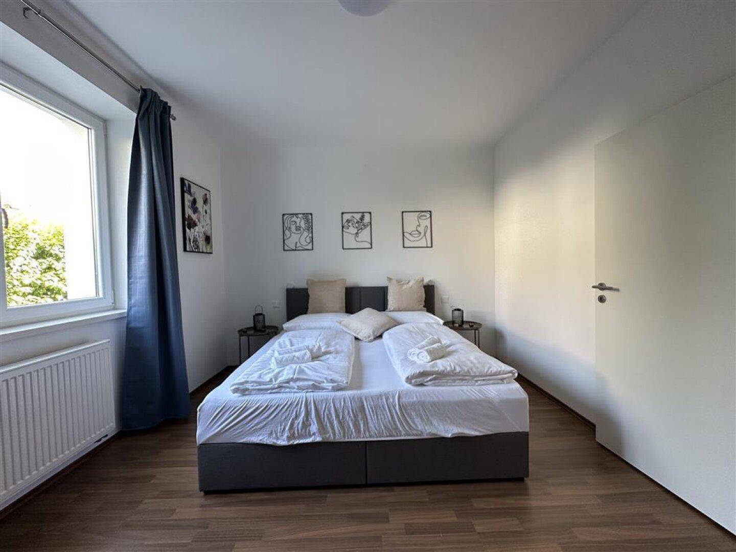 Helles Schlafzimmer mit Doppelbett, Holzfußboden und schlichten weißen Wänden, einladend gestaltet.