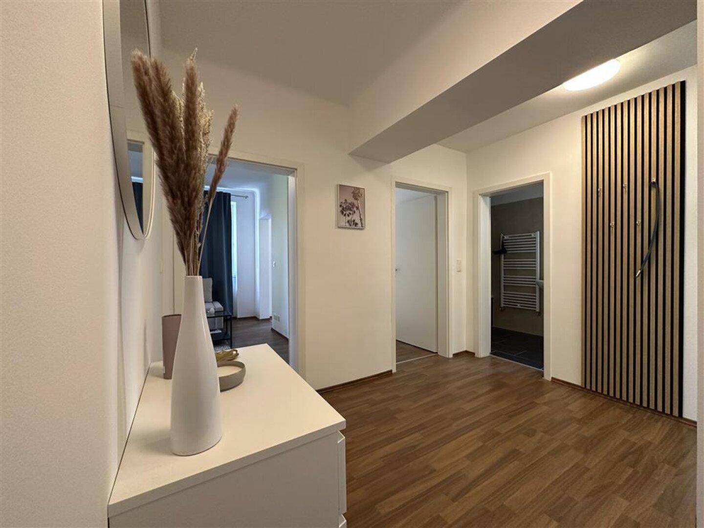 Moderner Flur mit Holzfußboden, vertikalen Holzlamellen und Zugang zu Bad und Schlafzimmer.