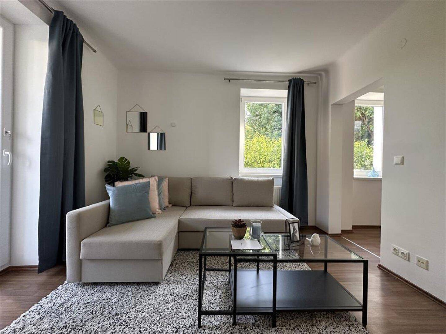 Gemütliches Wohnzimmer mit Ecksofa, Couchtisch und Zugang zur Terrasse mit Blick ins Grüne.