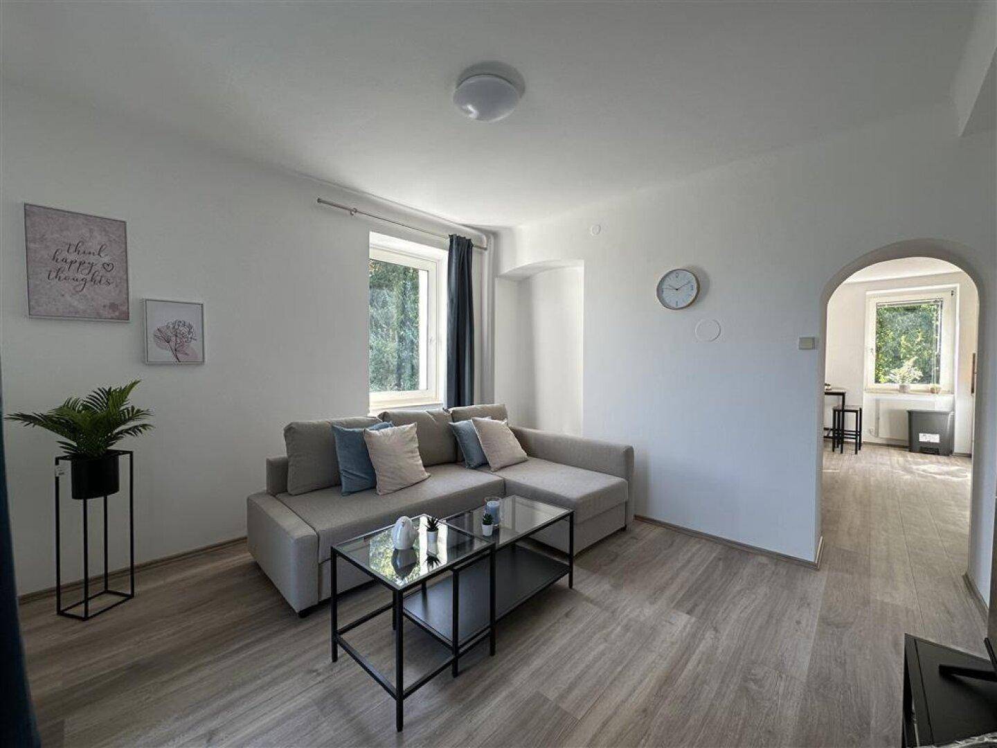 Helles Wohnzimmer mit Sofa, Couchtisch und Blick in einen weiteren Raum durch einen Rundbogen.