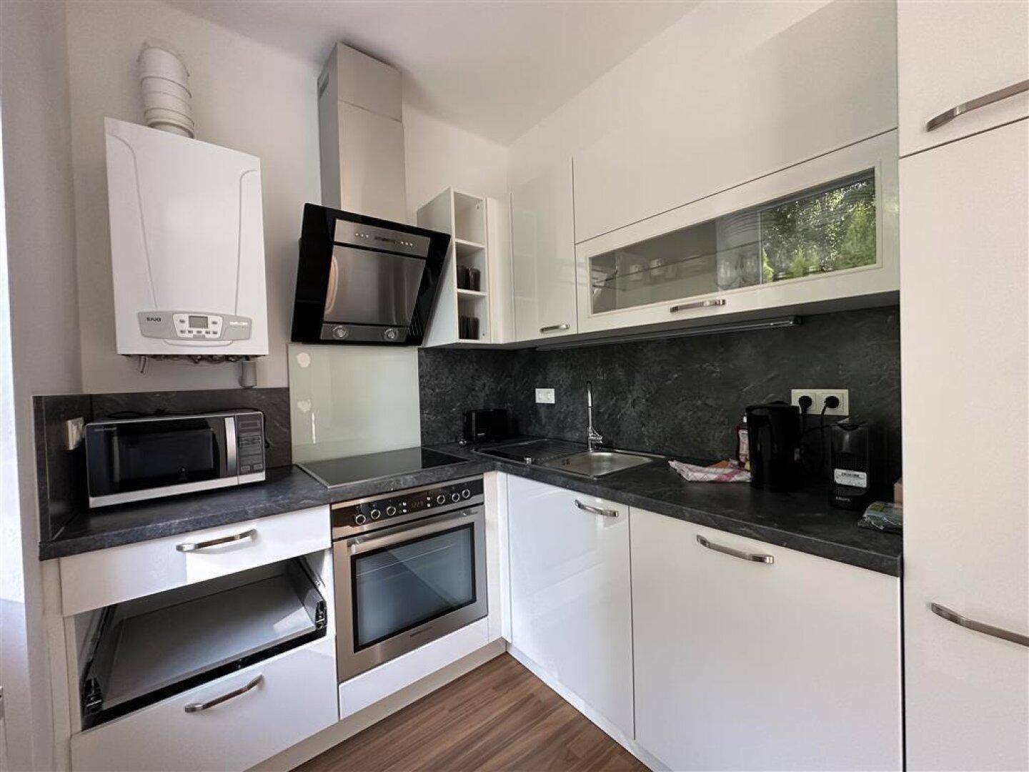 Moderne weiße Küche mit Hochglanzfronten, integrierten Geräten und dunkler Arbeitsplatte.
