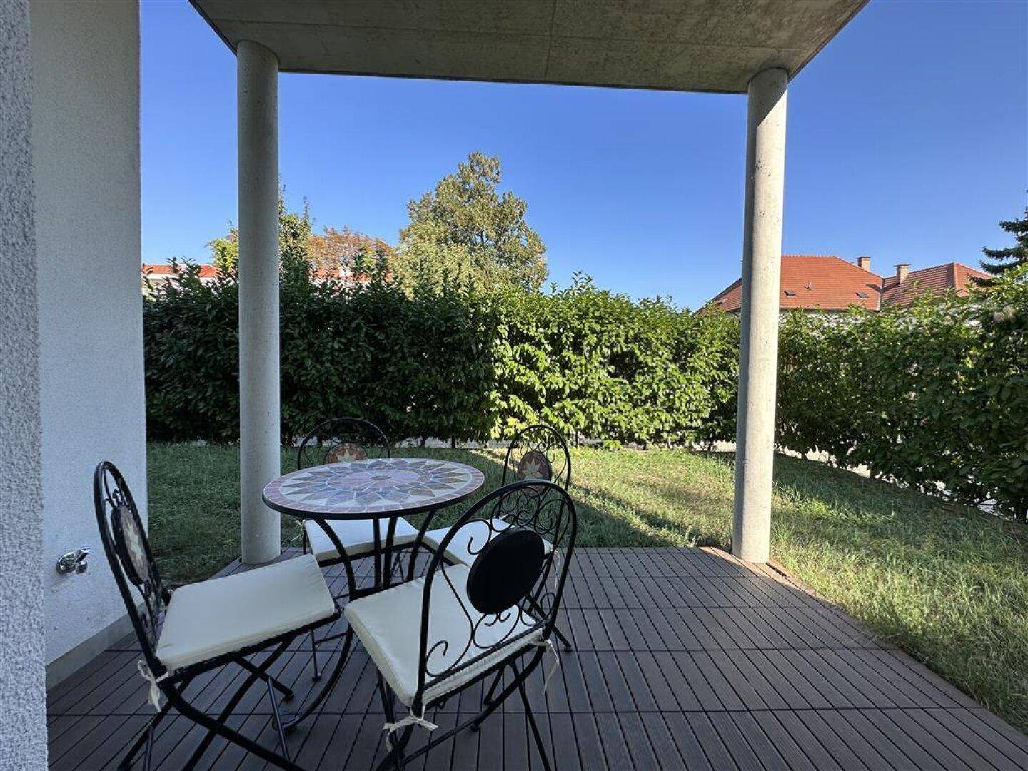 Überdachte Terrasse mit Gartenmöbeln und Blick auf eine gepflegte Hecke und Rasenfläche.