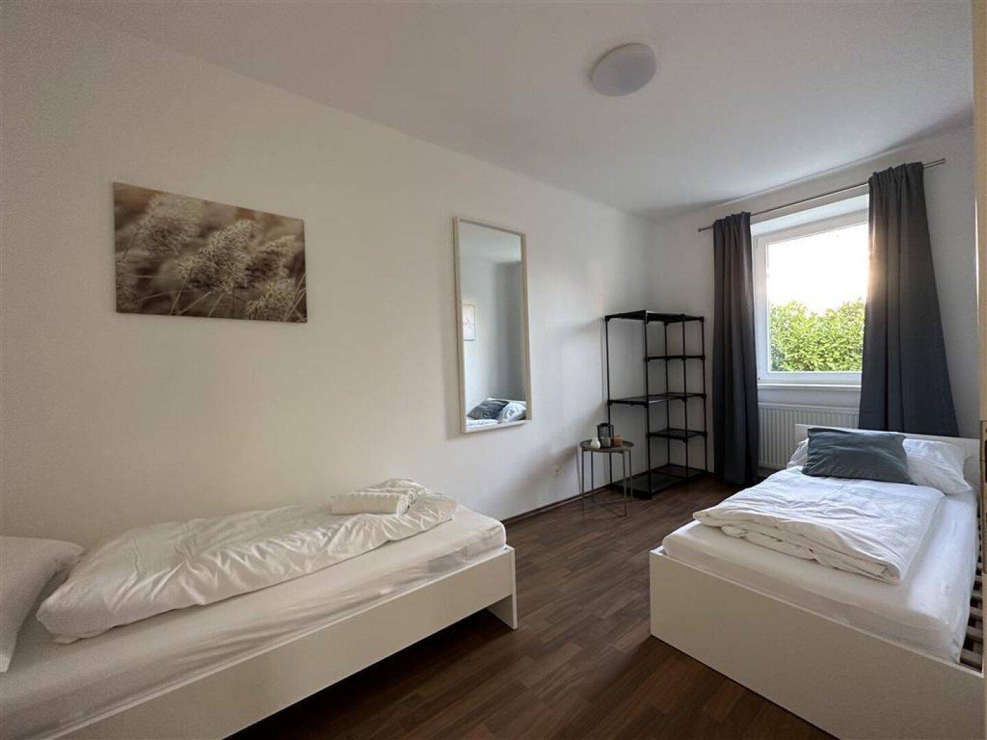 Schlafzimmer mit zwei Einzelbetten, Holzfußboden und Fenster mit Blick ins Grüne.