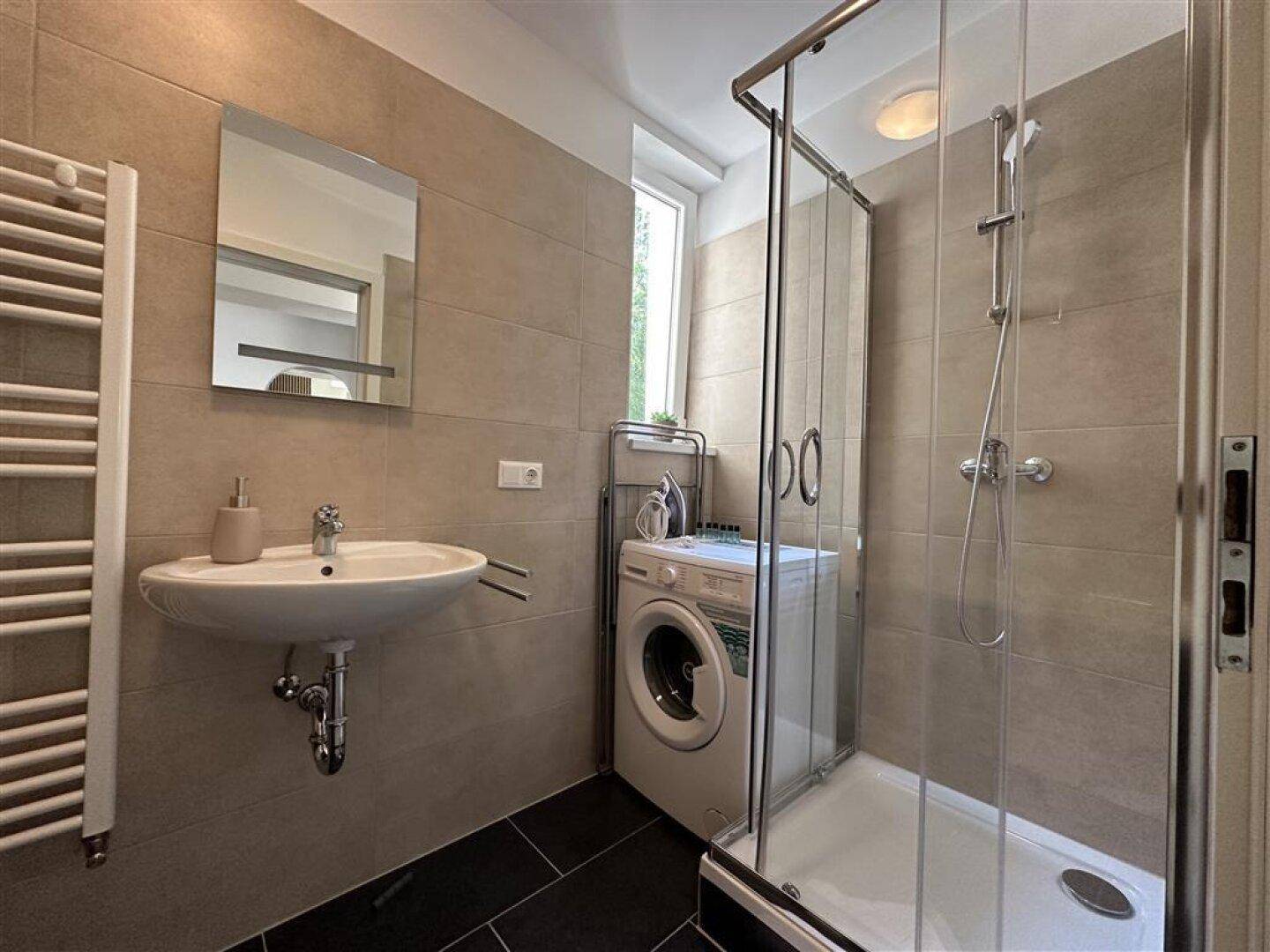 Modernes Badezimmer mit Dusche, Waschbecken, Waschmaschine und beheiztem Handtuchhalter.