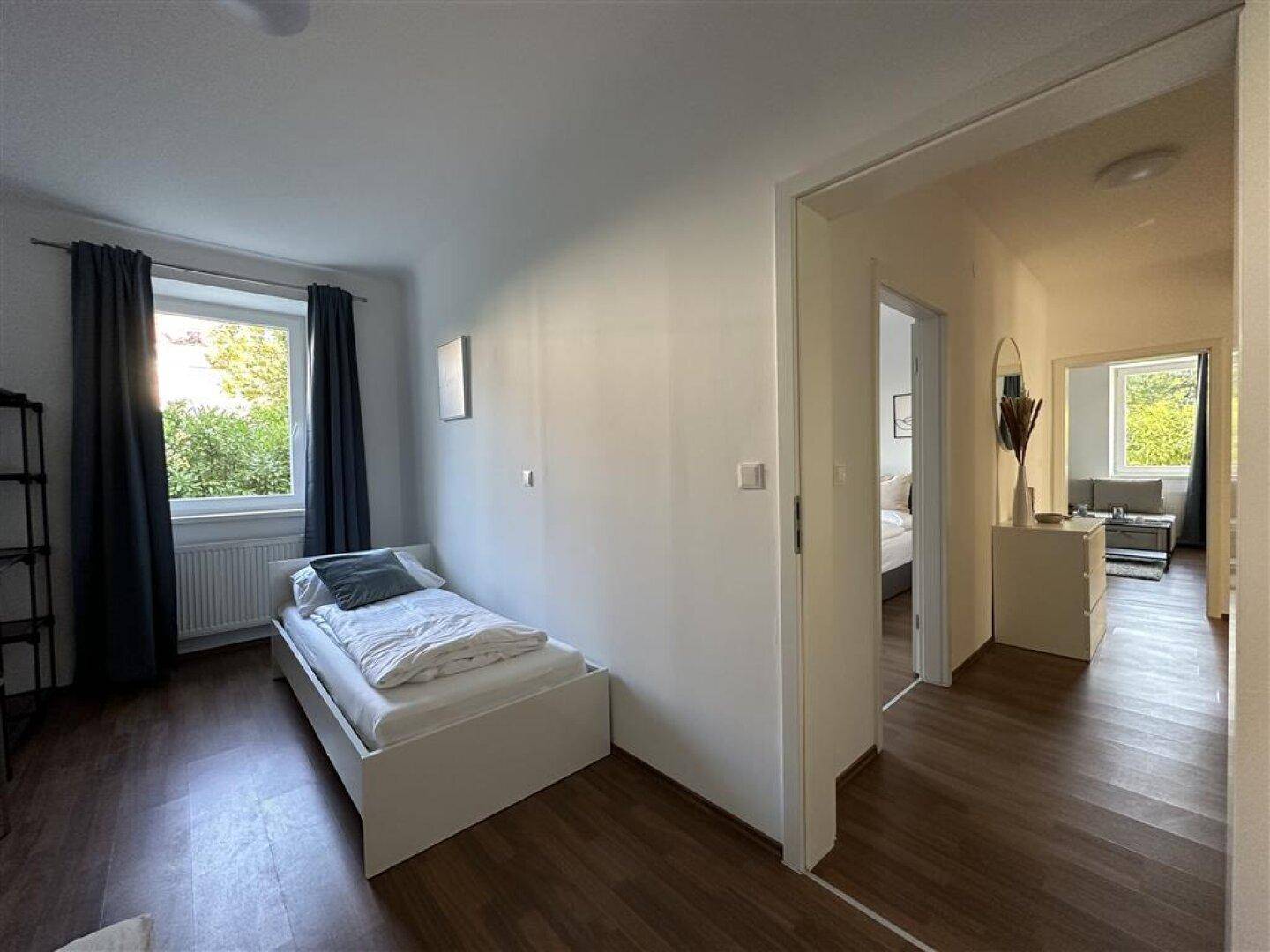 Helles Schlafzimmer mit Laminatboden, einem Einzelbett und Blick in den angrenzenden Flur.