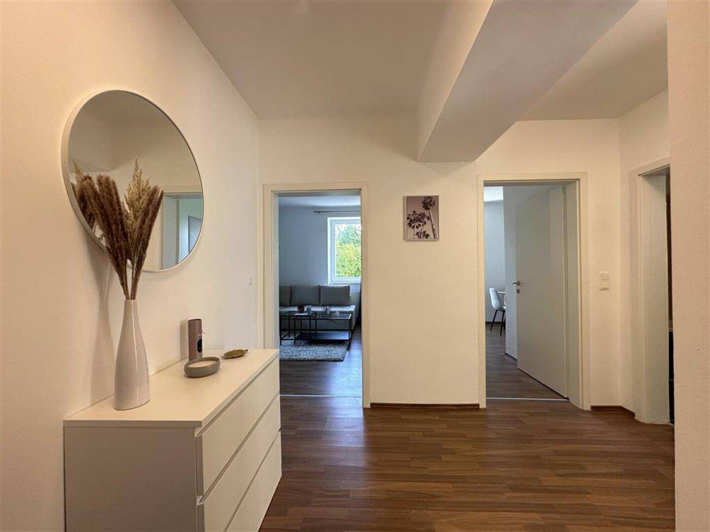 Geräumiger Flur mit hellem Holzfußboden und Blick in den Wohnbereich durch eine offene Tür.