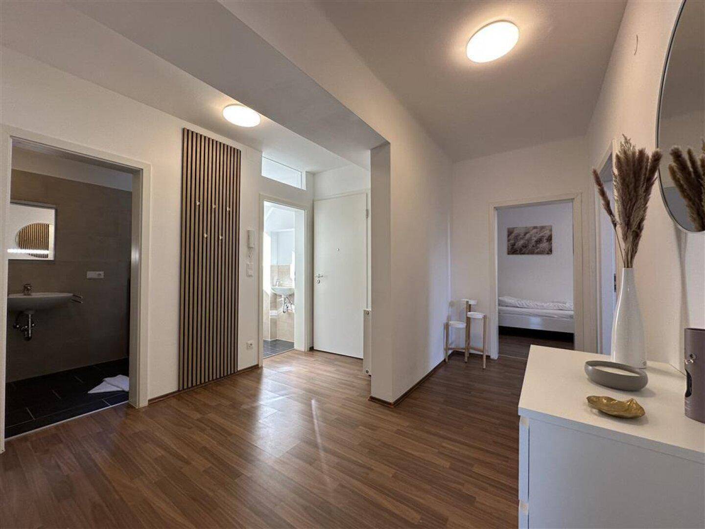 Heller Flur mit Holzfußboden, modernem Wandpaneel und Zugang zu verschiedenen Zimmern.