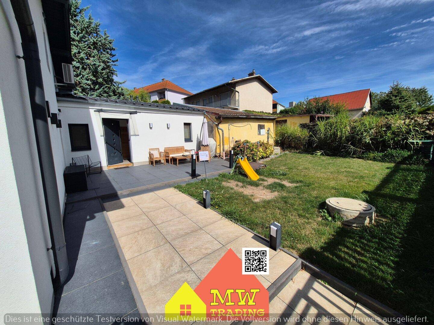 Gepflasterter Weg führt zur Terrasse und zum weitläufigen Gartenbereich mit Rasen und Spielgeräten.