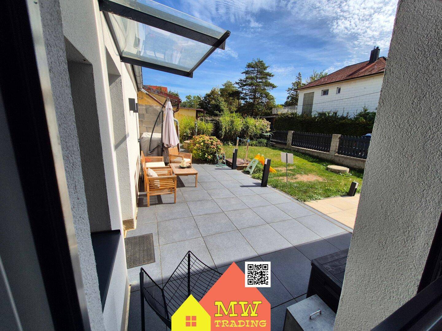 Geräumige Terrasse mit modernen Fliesen und Gartenmöbeln, angrenzend an den Garten.