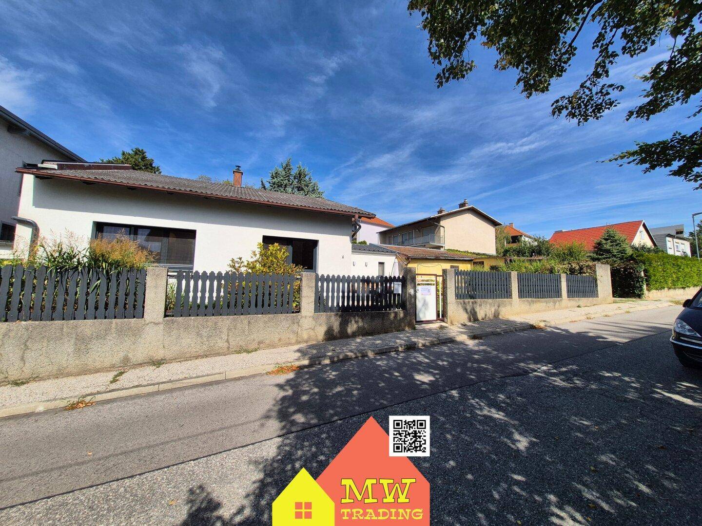 Ansicht des Hauses von der Straße mit einem Zaun und umliegenden Gebäuden.