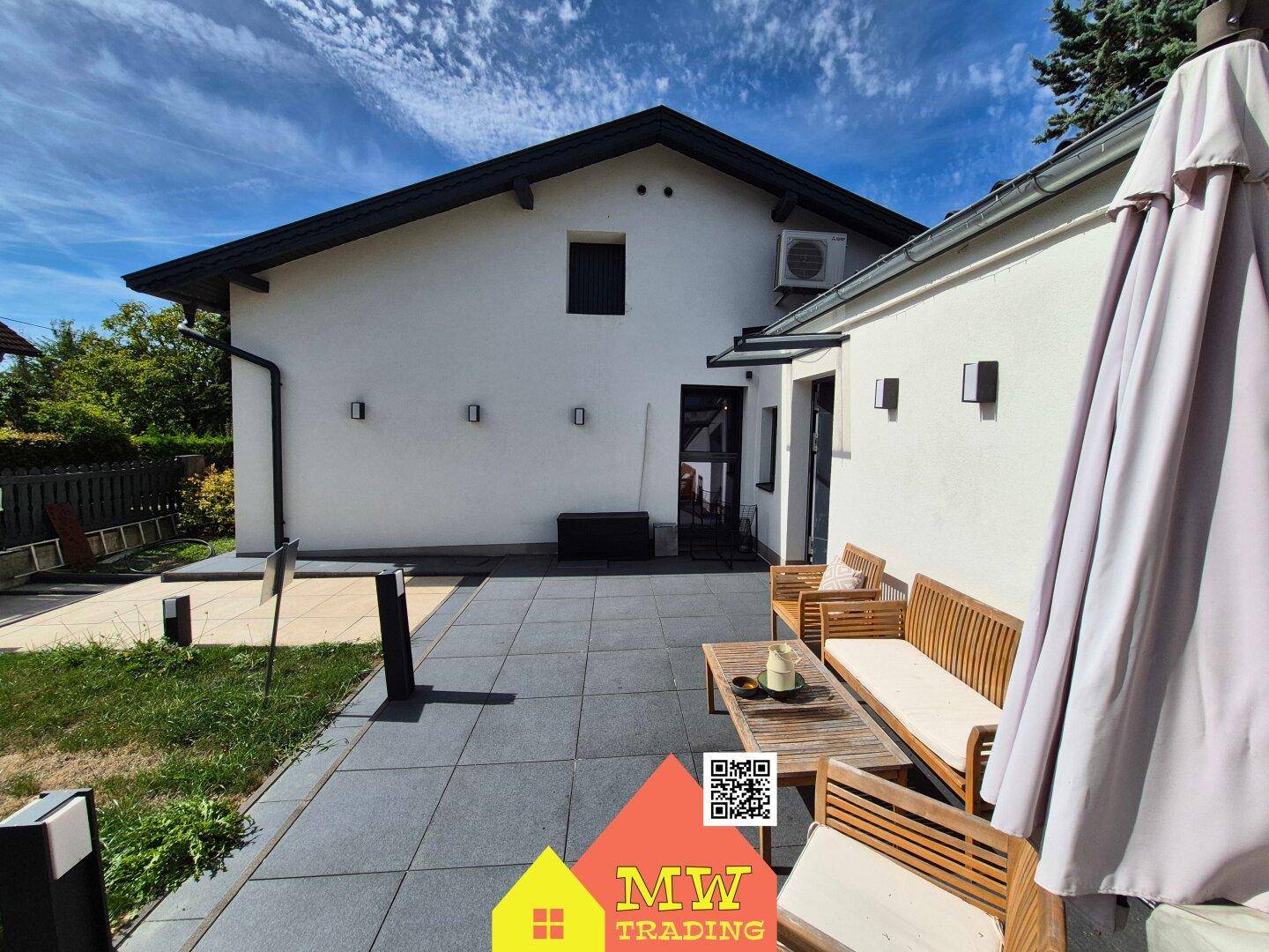 Rückansicht des Hauses mit großer, gepflasterter Terrasse und bequemen Gartenmöbeln.