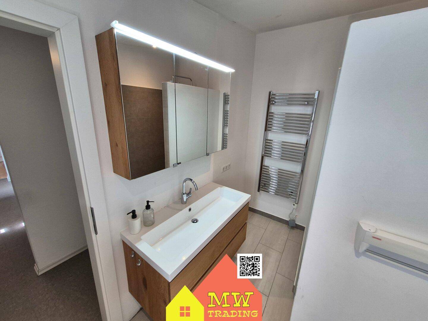 Badezimmer mit modernem Waschtisch, Spiegelschrank und beheiztem Handtuchhalter.