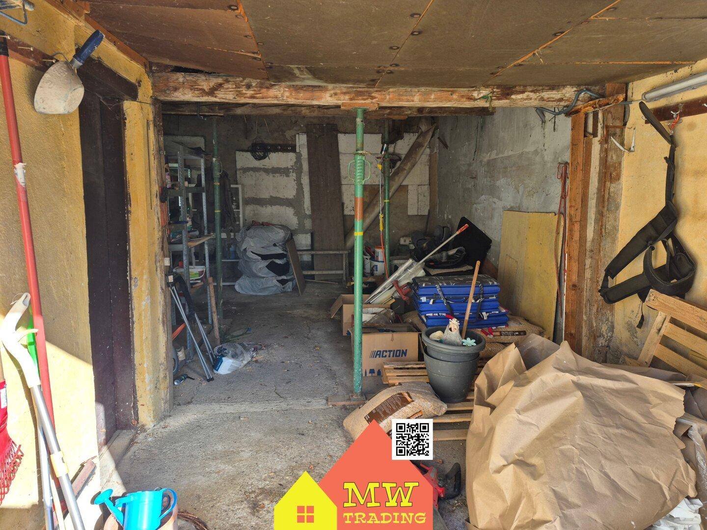 Unaufgeräumter Innenraum einer Garage oder eines Abstellraums mit Betonboden und sichtbaren Balken.