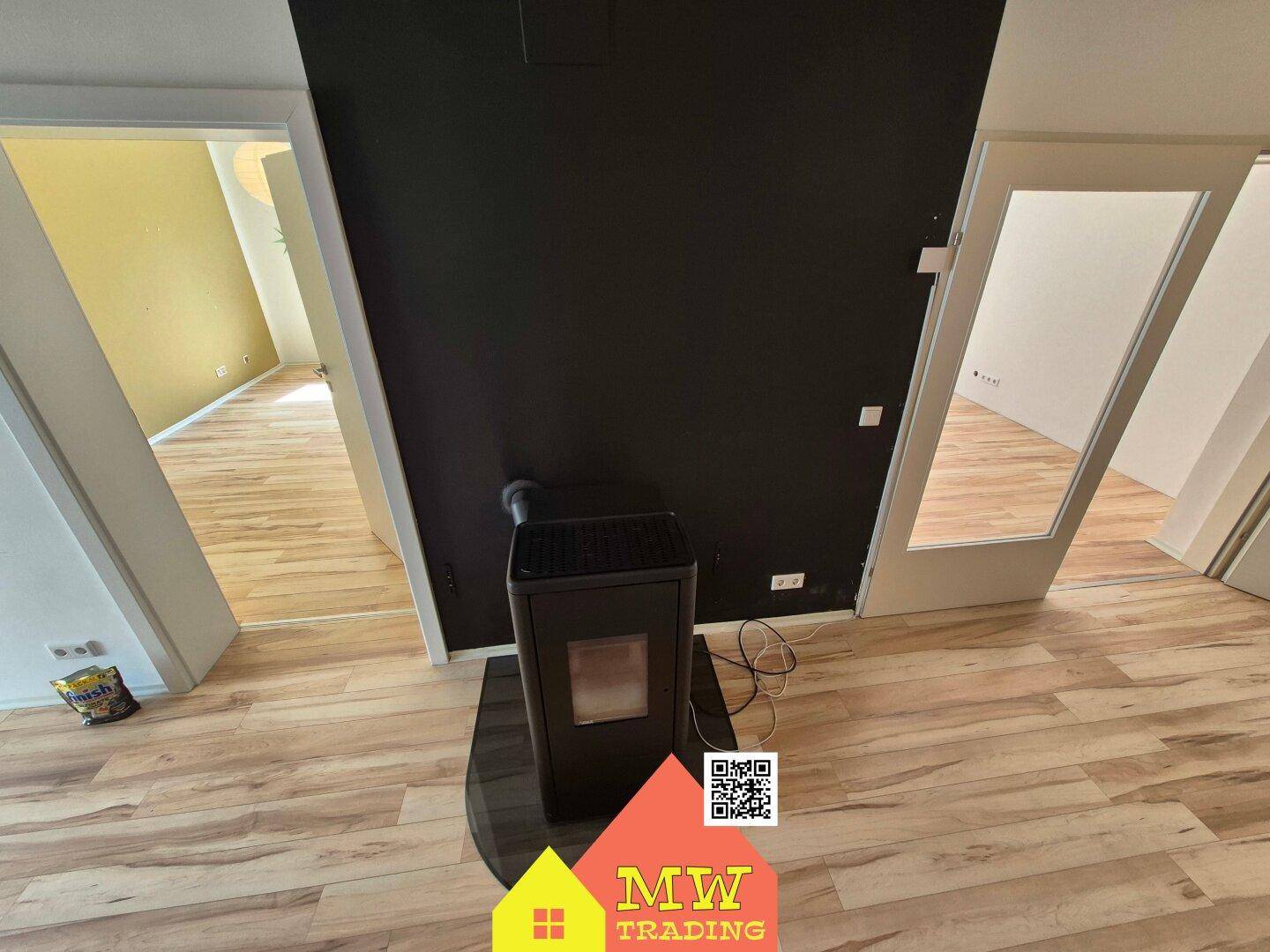 Moderner Kaminofen im offenen Wohnbereich, umgeben von Holzboden und dunkler Wand.