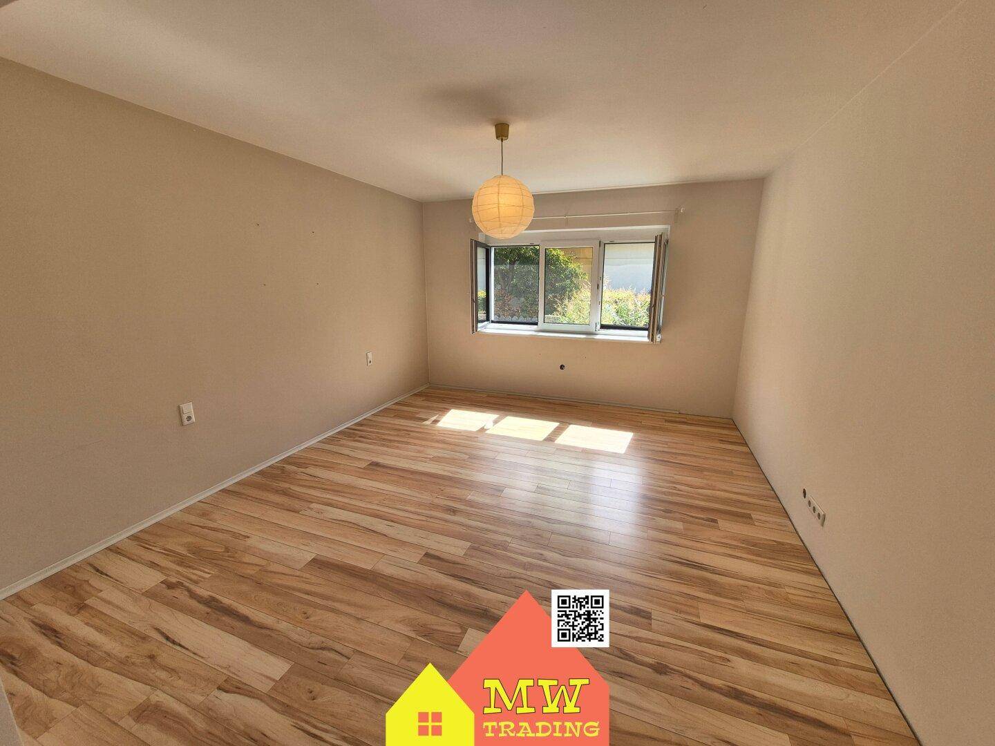 Helles Schlafzimmer mit Holzboden und großem Fenster, das viel Tageslicht hereinlässt.