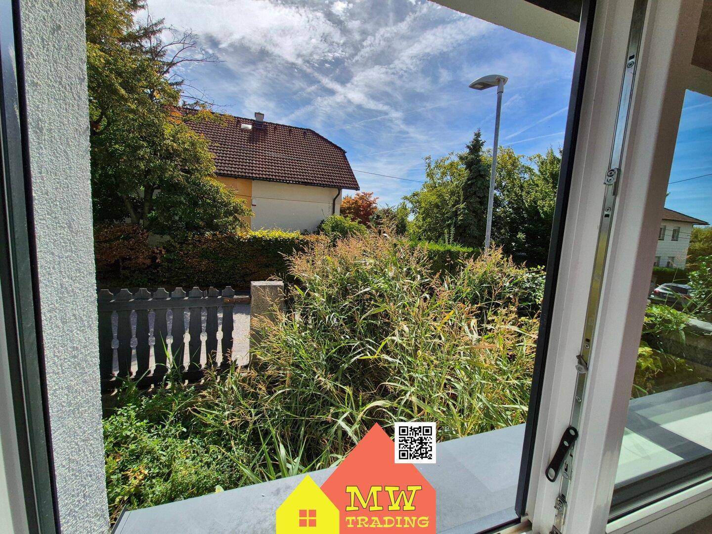 Blick aus dem Fenster auf die grüne Umgebung und ein benachbartes Haus.