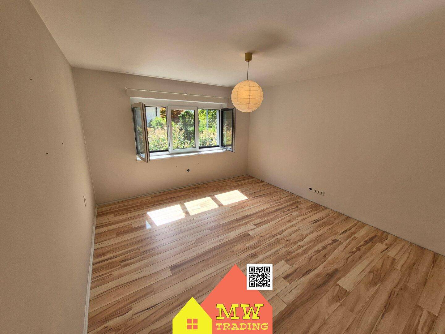 Helles Schlafzimmer mit Holzboden und Fenster, das den Raum mit Tageslicht füllt.