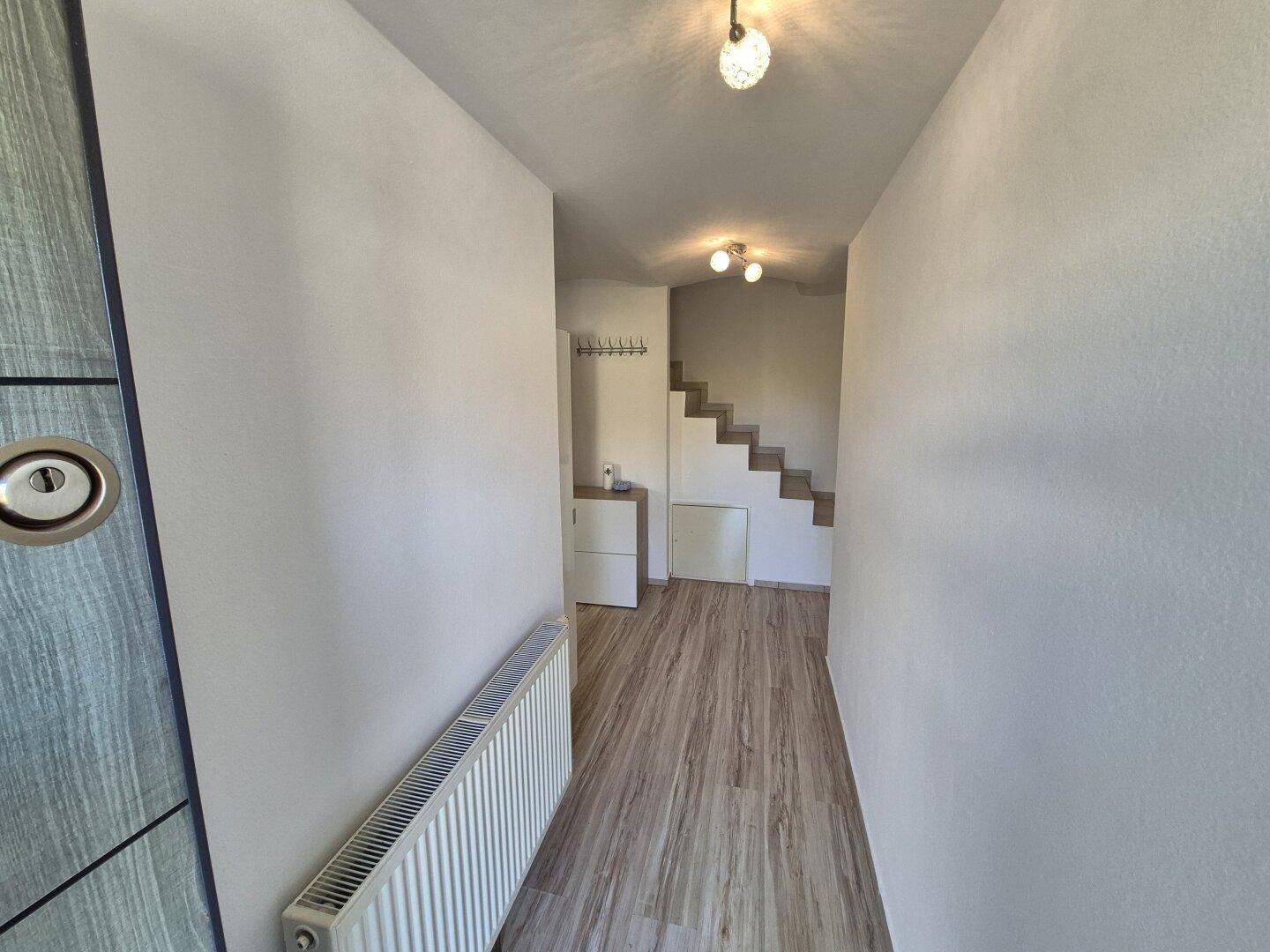 Heller Flur mit Holzoptik-Boden, Heizkörper und Treppe, die in die obere Etage führt.