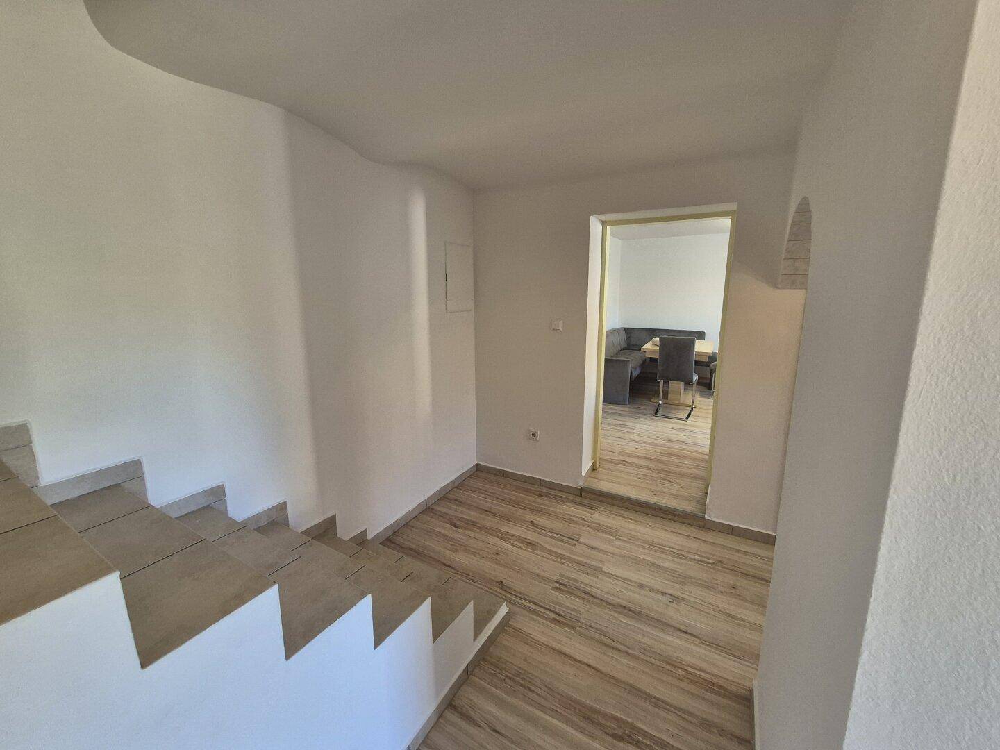 Flur mit Treppe und Blick in einen angrenzenden Raum, ausgestattet mit Holzoptik-Boden.