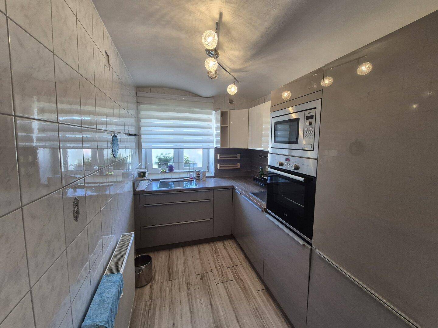 Moderne Küche mit hellen Schränken, integrierten Geräten und einem Fenster mit Jalousie.