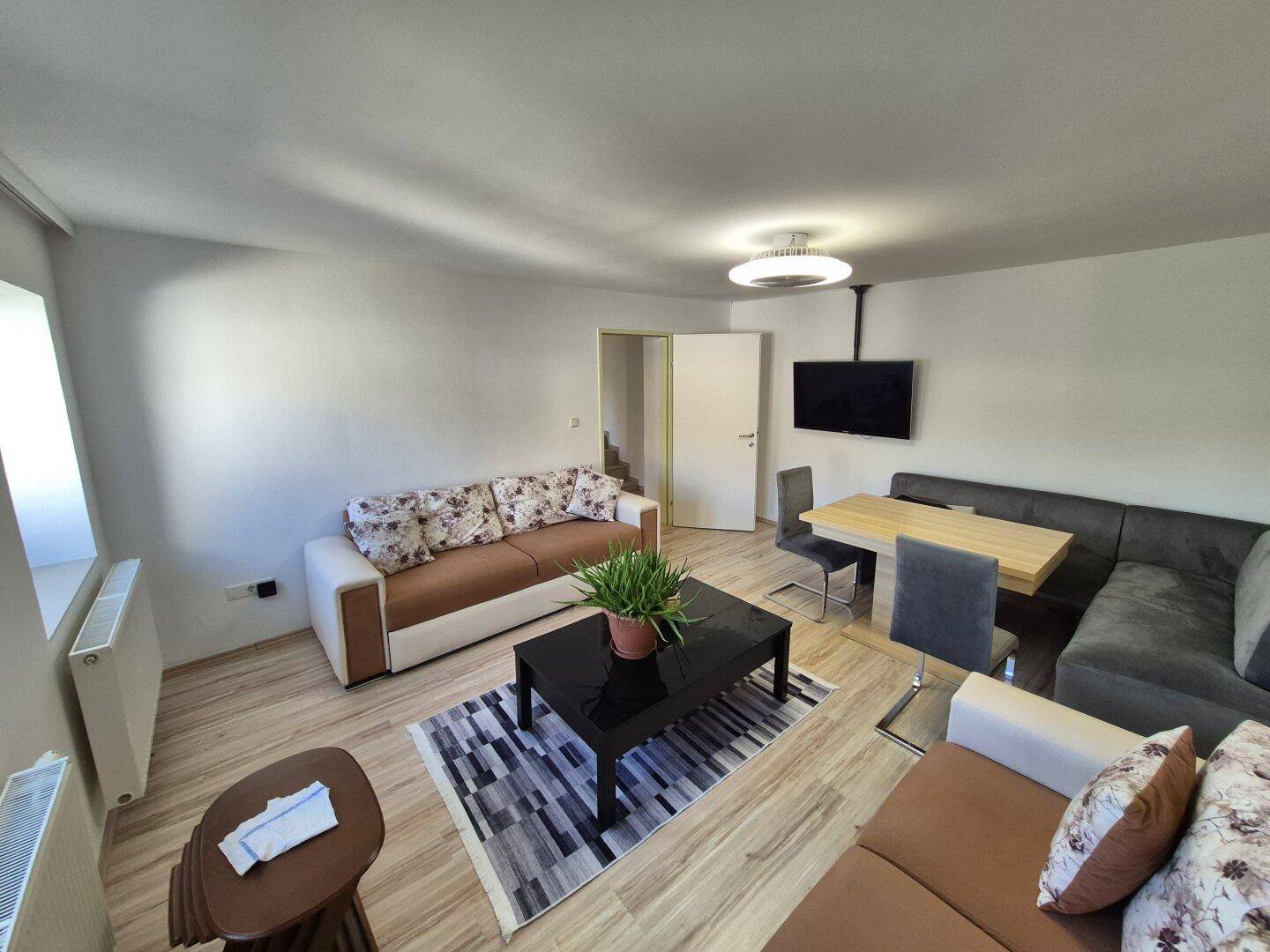 Geräumiger Wohn- und Essbereich mit Wandfernseher, modernen Sofas und einem Esstisch.