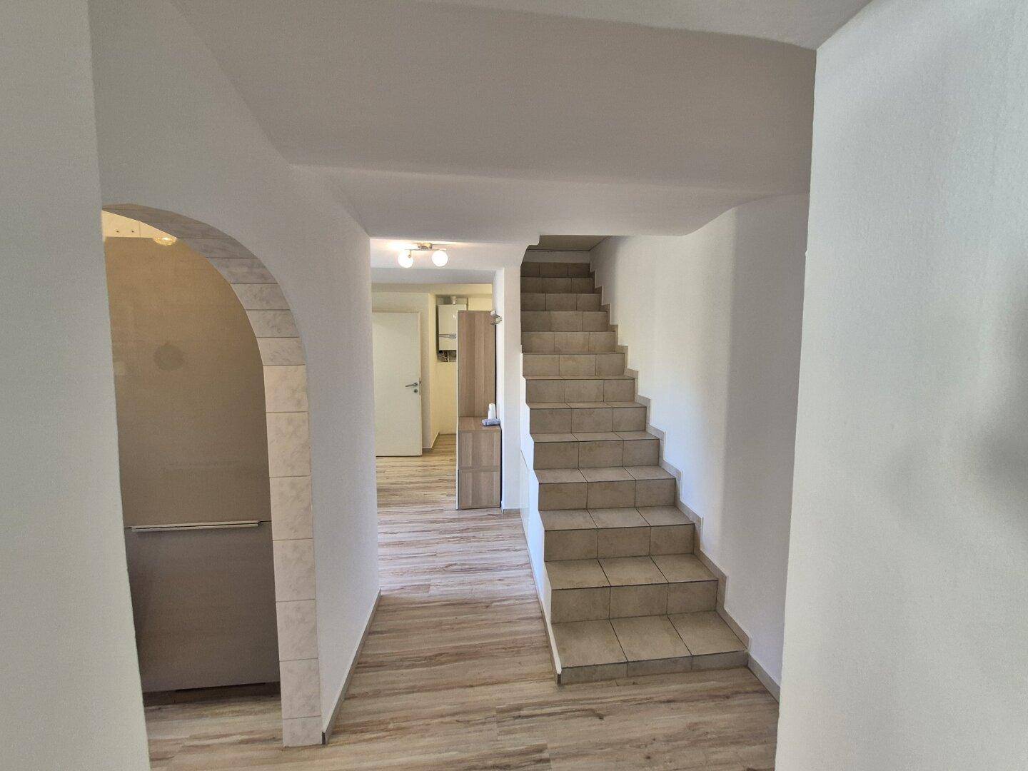 Flur mit Treppe, die mit Fliesen belegt ist, und einem eleganten Bogen zu einem weiteren Bereich.