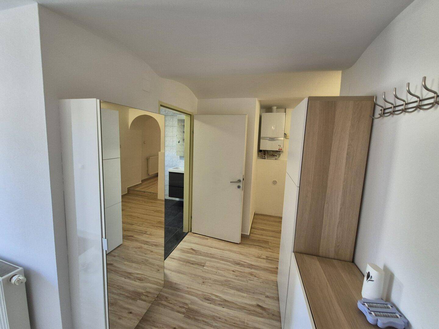 Eingangsbereich mit Spiegelschrank, Garderobe und Blick in einen angrenzenden Raum.
