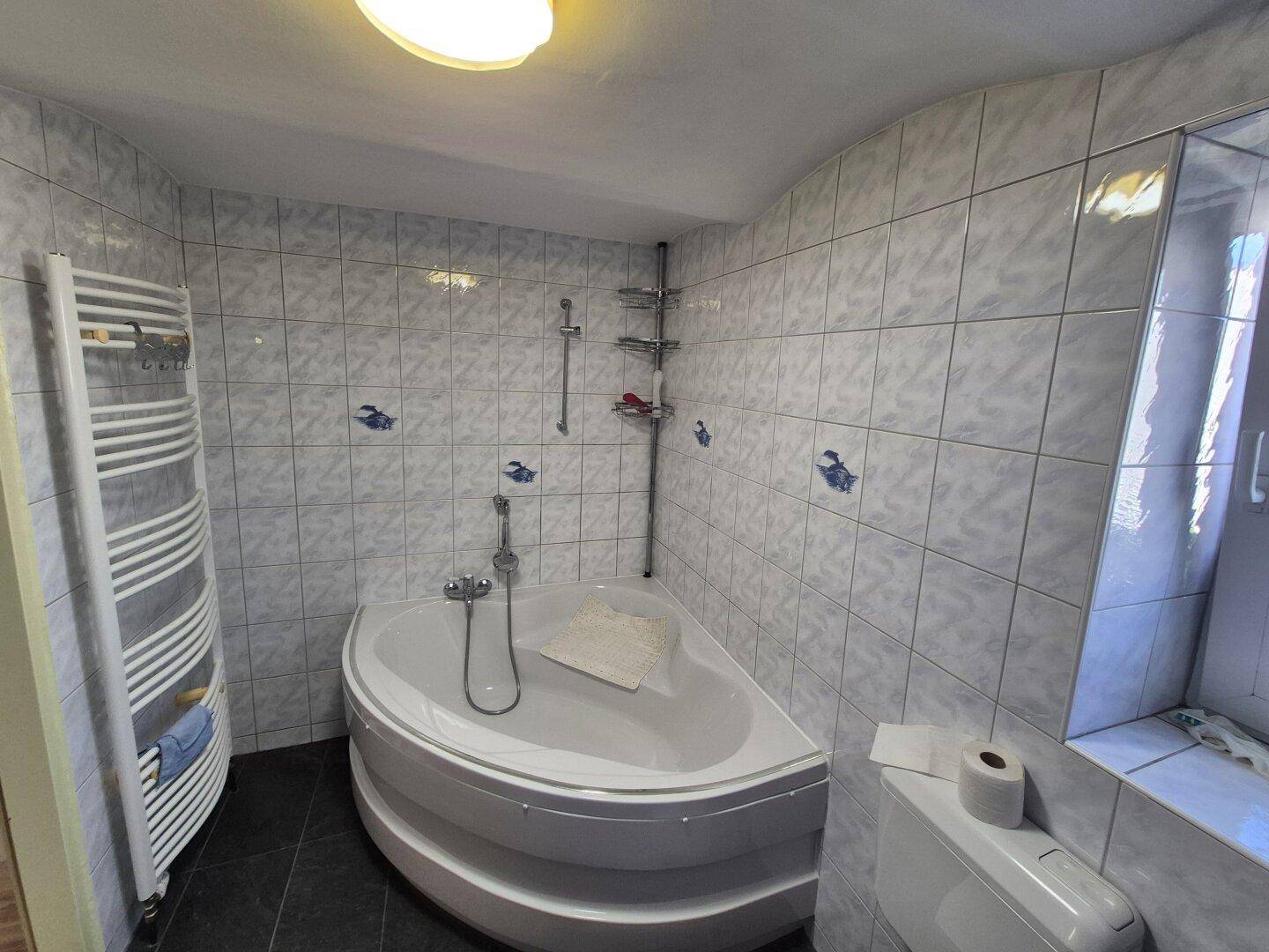 Badezimmer mit Eckbadewanne, Handtuchheizkörper und hellen Fliesen, gut beleuchtet.