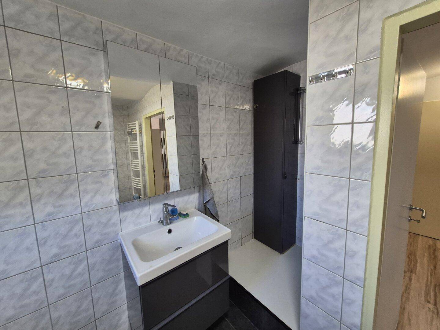 Badezimmer mit modernem Waschtisch, Spiegelschrank und hellen Fliesen an den Wänden.
