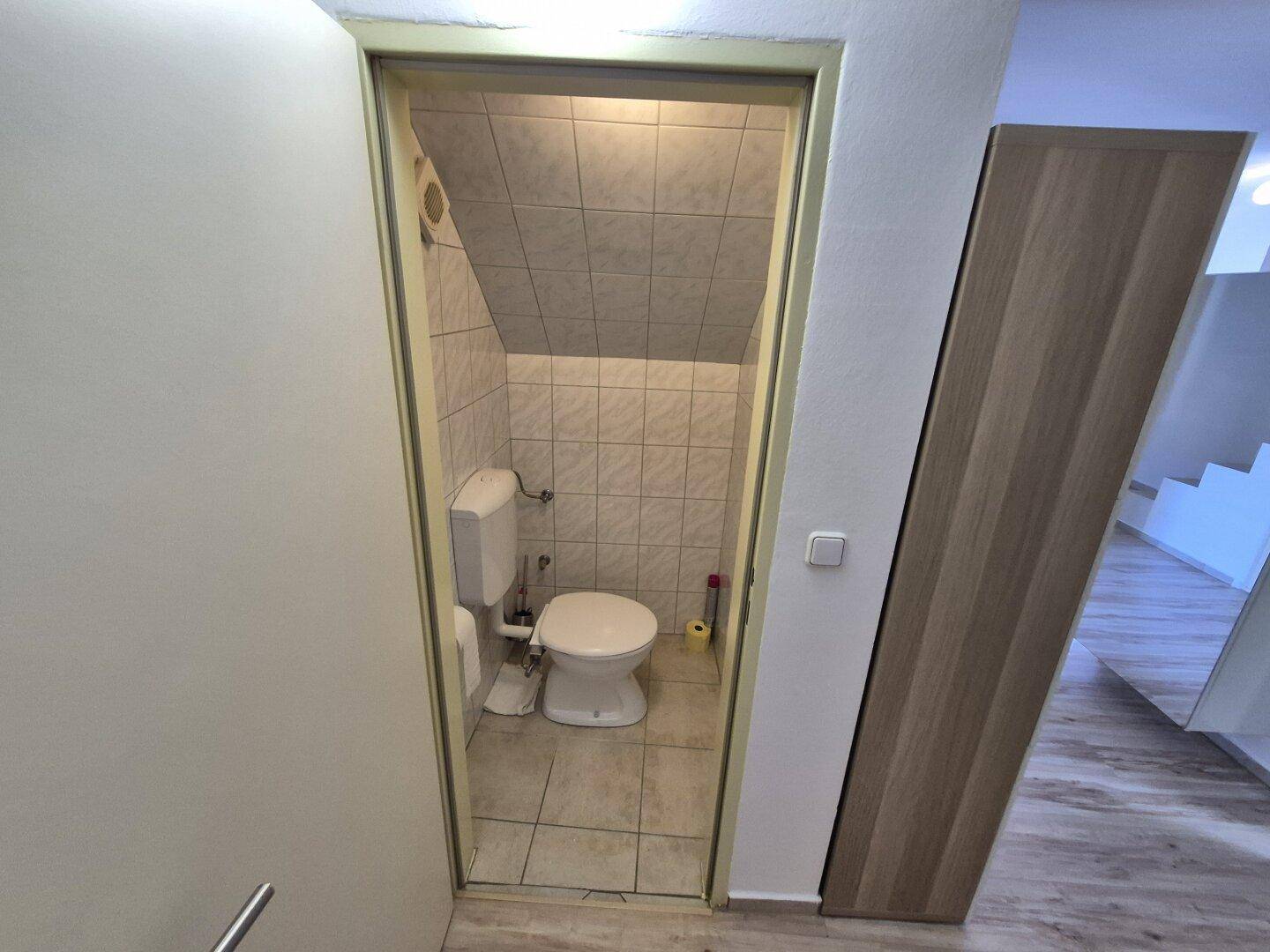 Kleines Gäste-WC mit Toilette und Fliesen unter einer Dachschräge, funktional eingerichtet.
