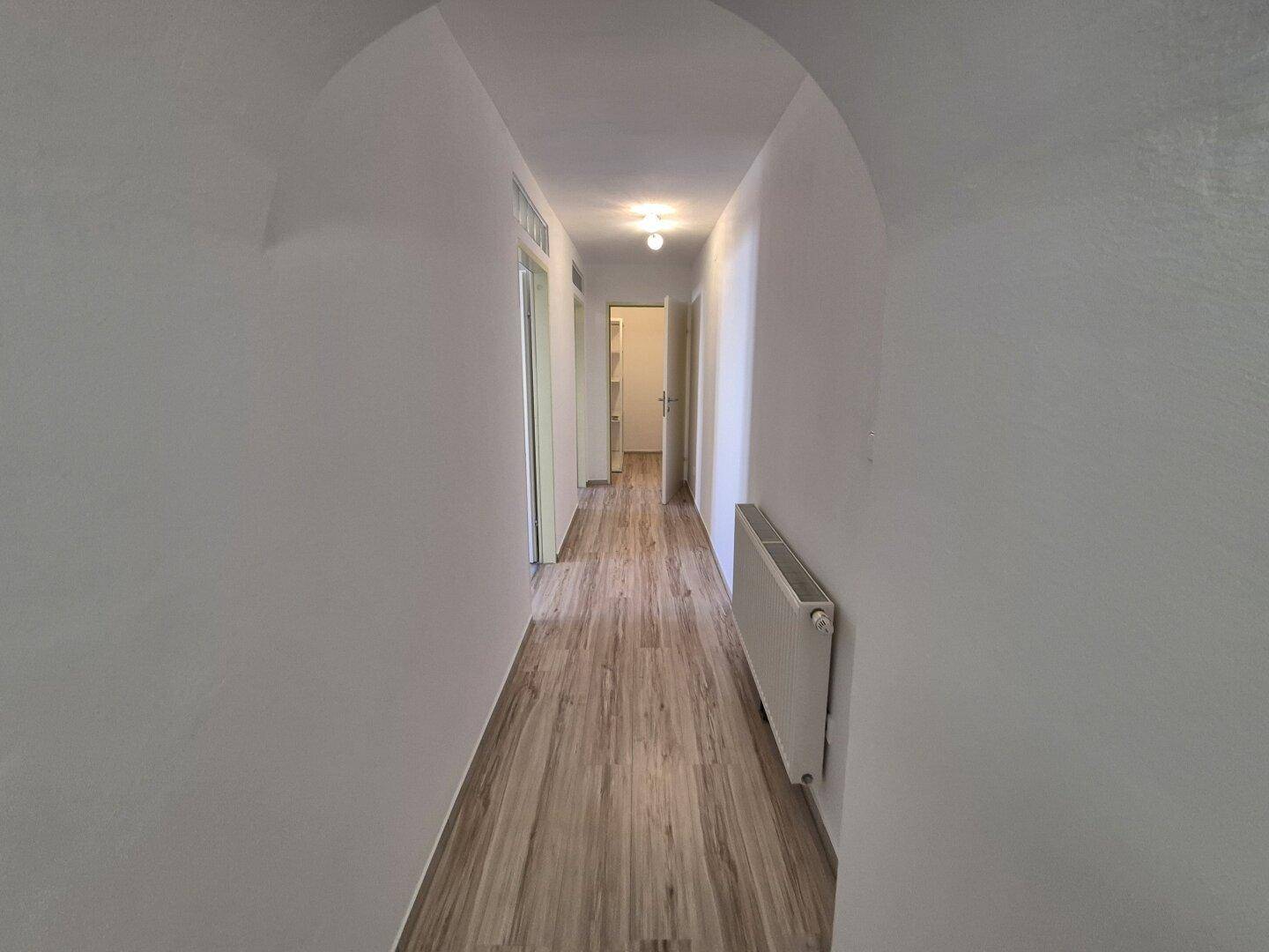 Langer, heller Flur mit Holzoptik-Boden und einem Heizkörper an der Wand, gut beleuchtet.