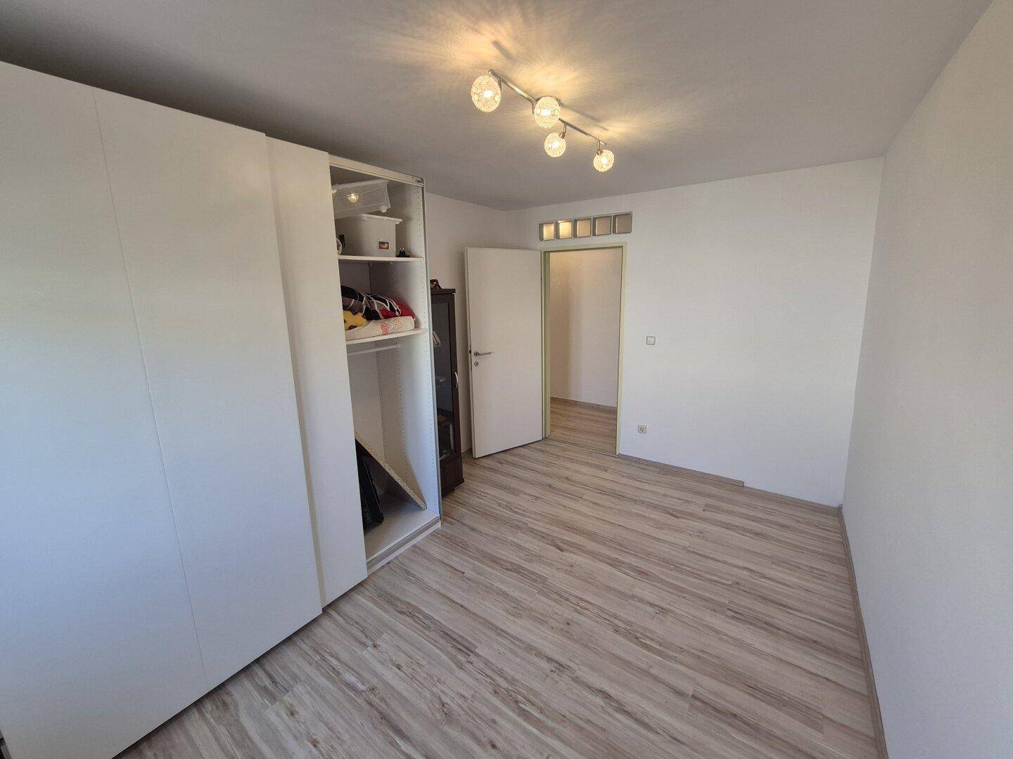 Helles Schlafzimmer mit weißem Schiebetürenschrank, Laminatboden und Deckenleuchte.