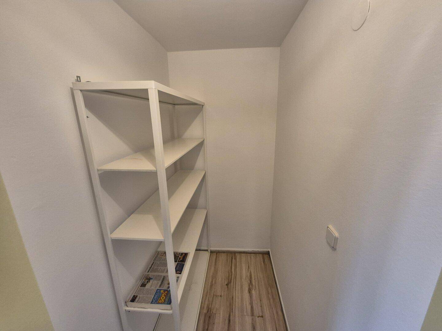 Praktischer Abstellraum mit weißem Metallregal und hellem Laminatboden für zusätzlichen Stauraum.