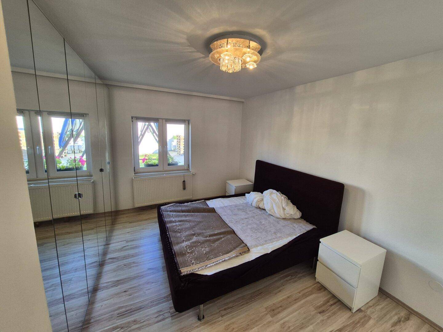Gemütliches Schlafzimmer mit Doppelbett, Spiegelschrank und zwei Fenstern für viel Tageslicht.
