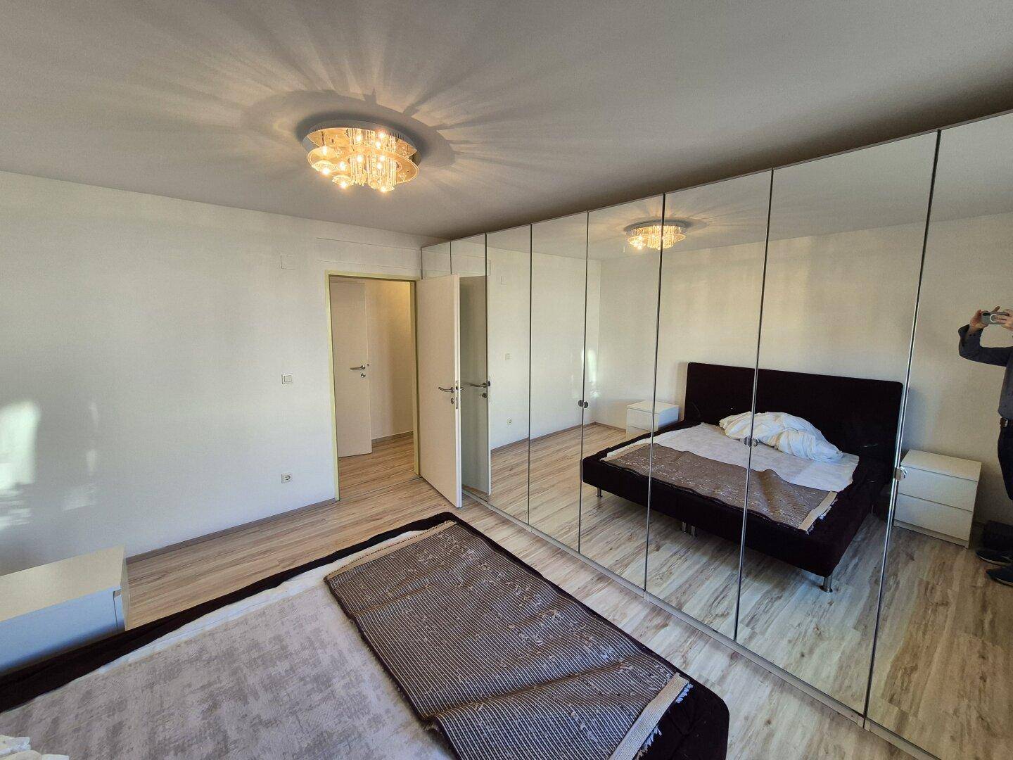 Schlafzimmer mit großem Spiegelschrank, Doppelbett und Zugang zu einem angrenzenden Raum.