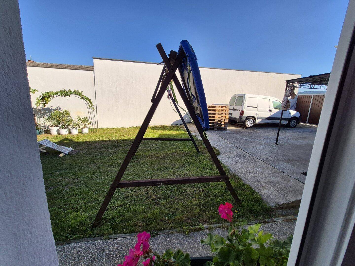 Kleiner Gartenbereich mit Rasen, Schaukel und gepflastertem Hof, ideal für Freizeitaktivitäten.