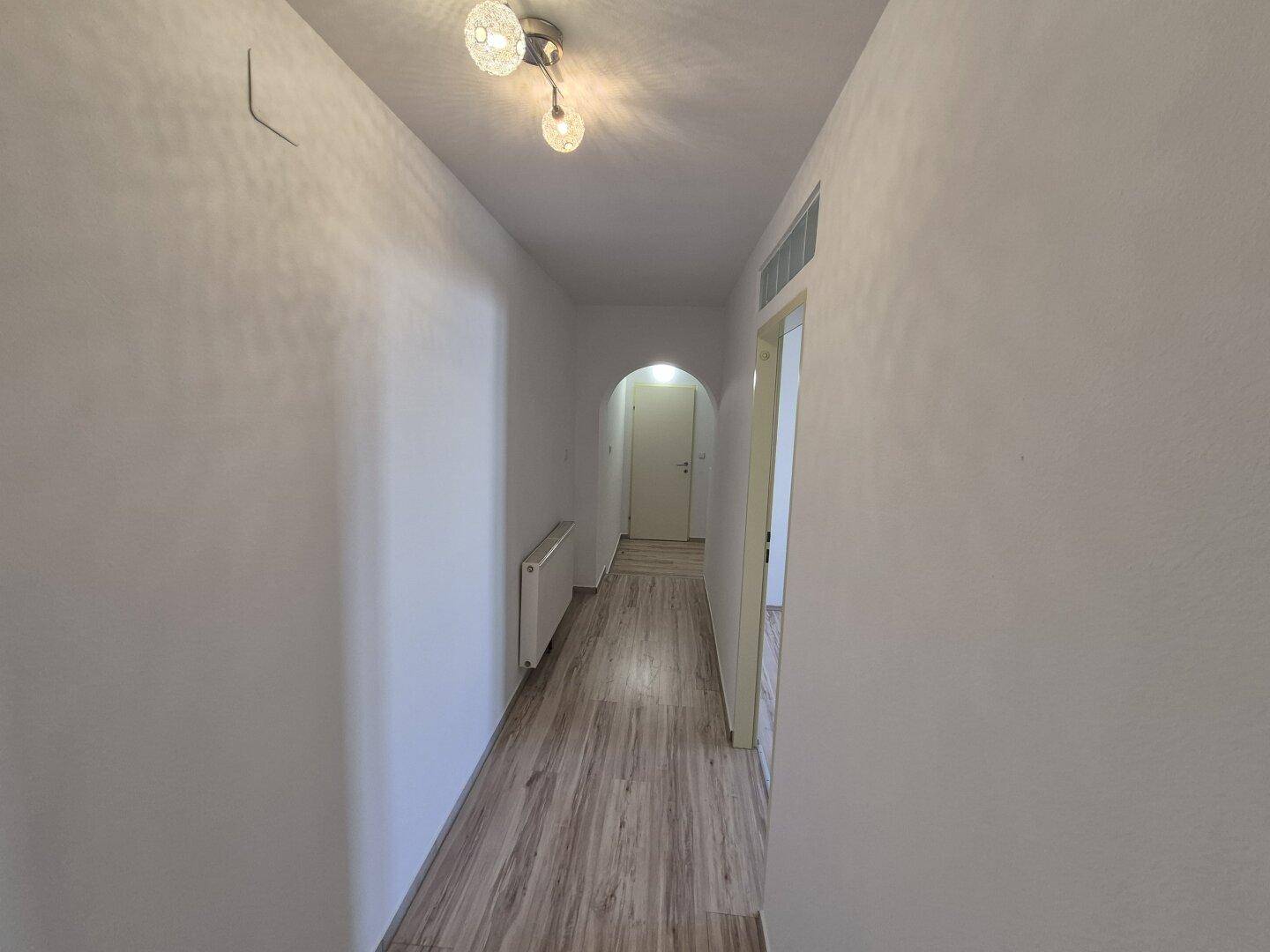 Heller Flur mit Laminatboden und weißen Wänden, der einen Zugang zu anderen Räumen bietet.