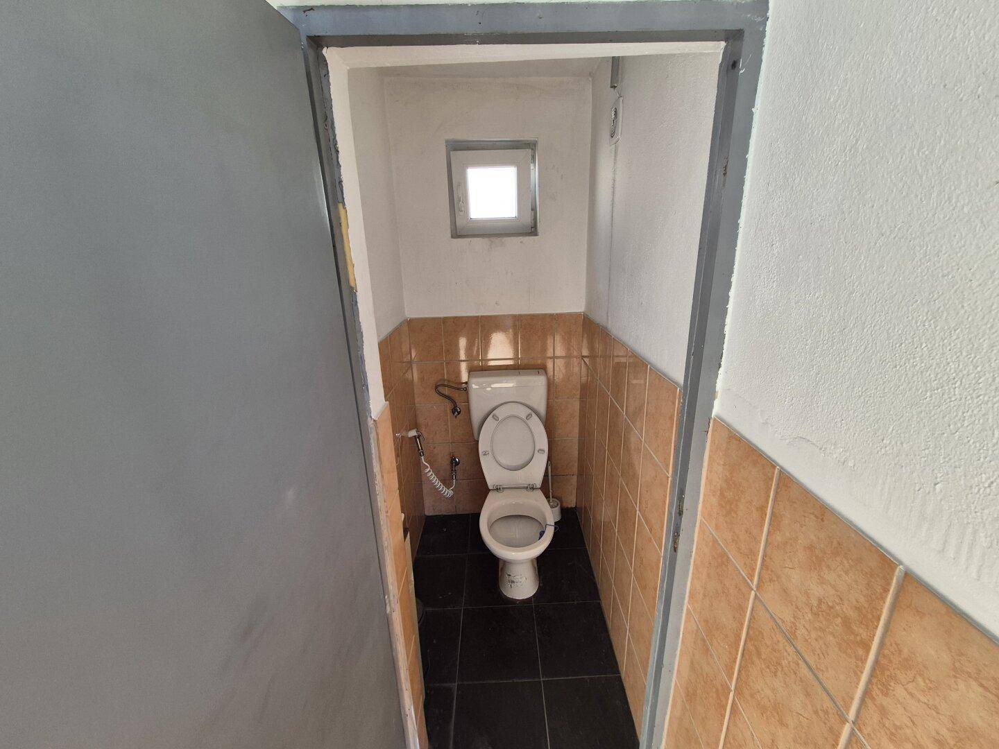 Einfache Gästetoilette mit kleinem Fenster, braunen Wandfliesen und dunklem Fliesenboden.