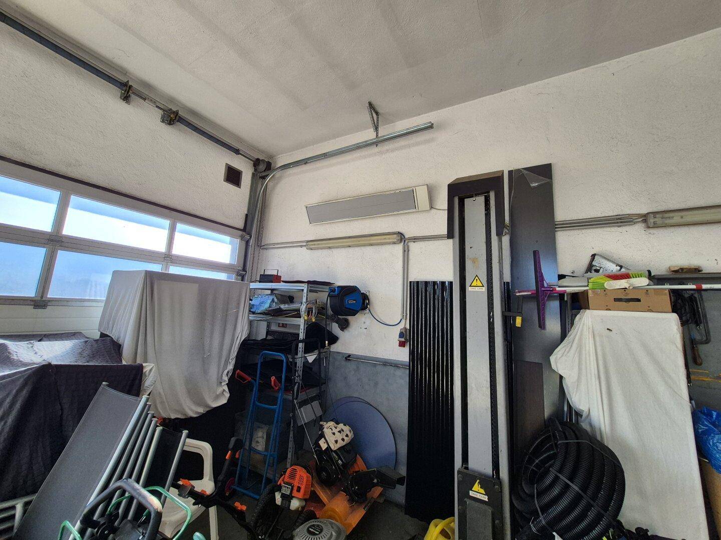 Innenansicht einer Garage oder Werkstatt mit Rolltor und verschiedenen Werkzeugen und Geräten.