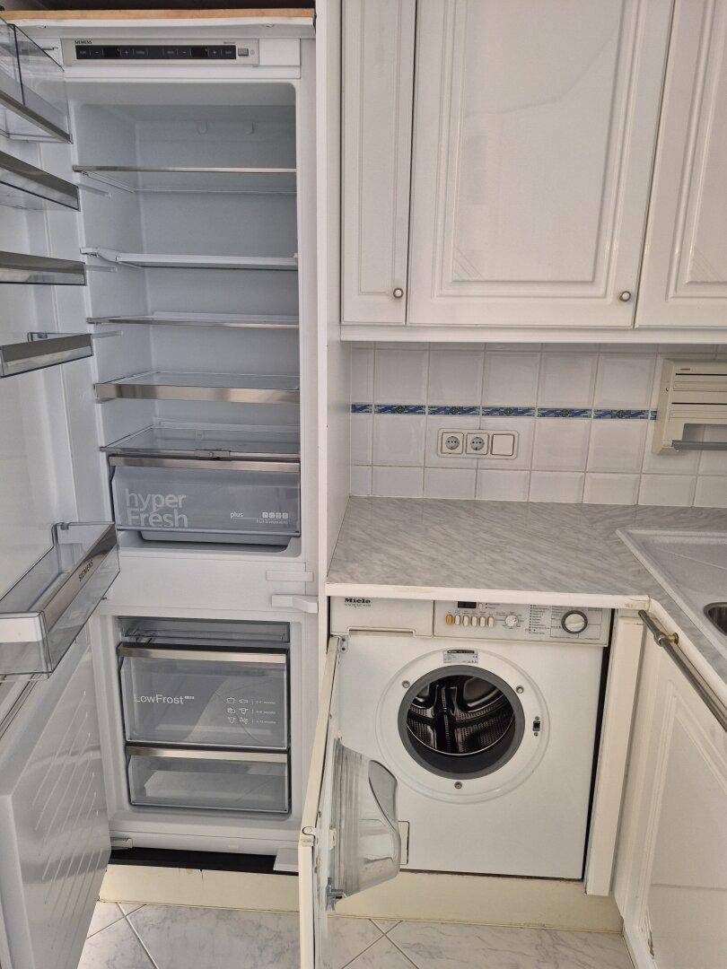 Integrierter Kühlschrank und Waschmaschine in der weißen Einbauküche mit Marmorarbeitsplatte.
