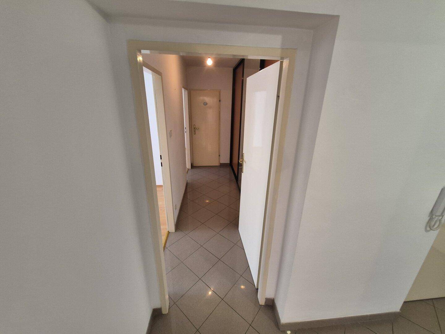 Langer Flur mit Fliesenboden und Türen, die zu verschiedenen Bereichen der Wohnung führen.
