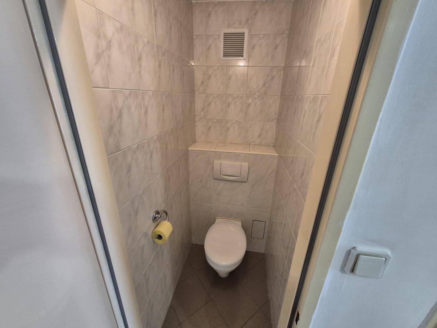 Separate Toilette mit Wand-WC und Fliesen an Wänden und Boden in hellem Design.