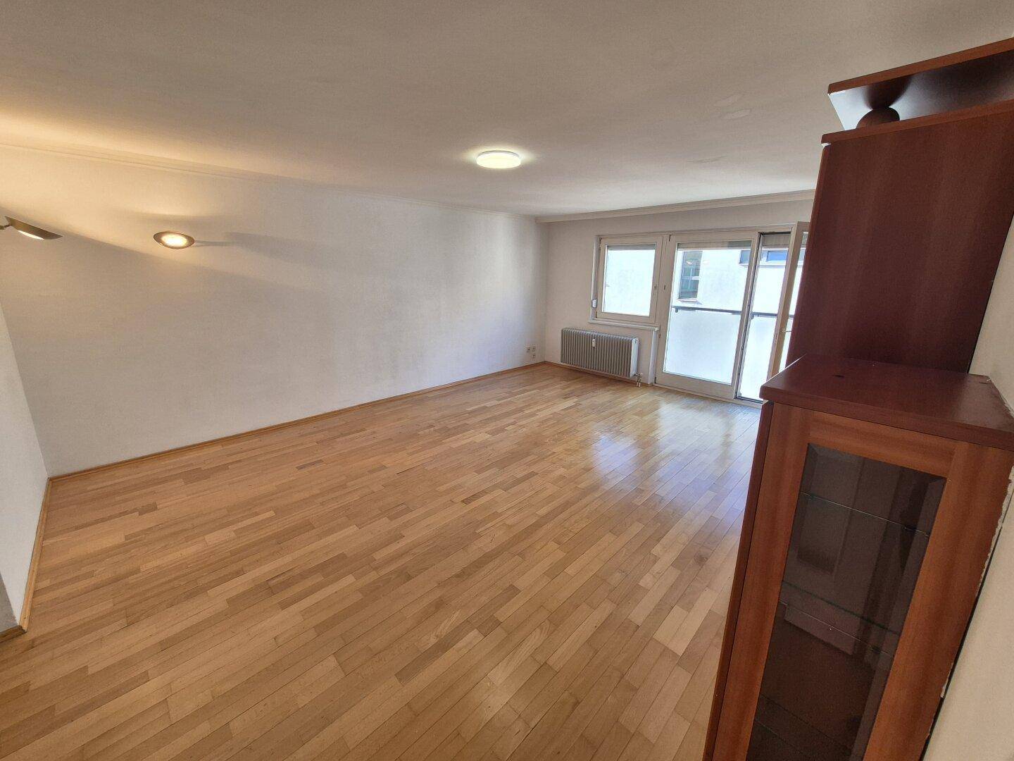 Geräumiges Wohnzimmer mit hellem Parkettboden und Zugang zu einem Balkon oder einer Terrasse.
