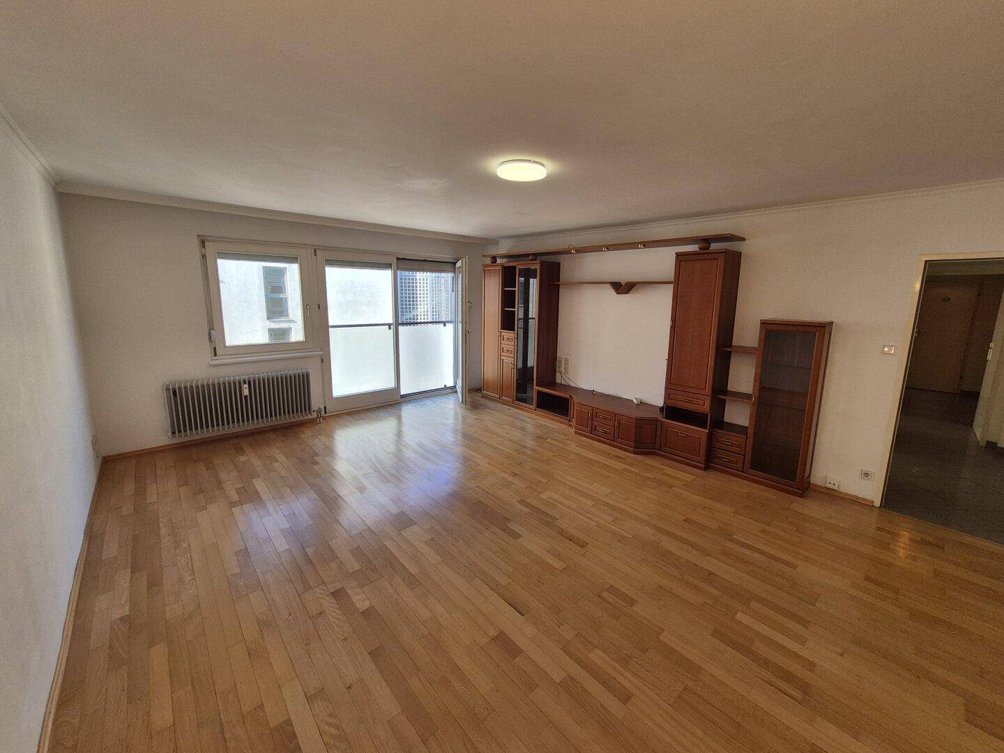Helles Wohnzimmer mit Parkettboden und einer großen Schrankwand, die viel Stauraum bietet.