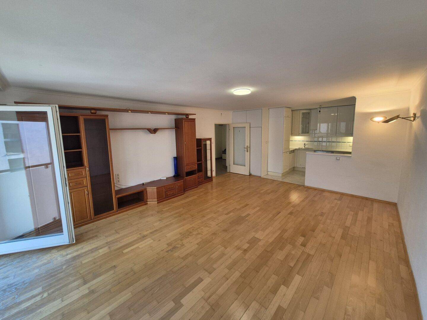 Offener Wohnbereich mit Parkettboden und integrierter Küchenzeile im Hintergrund.