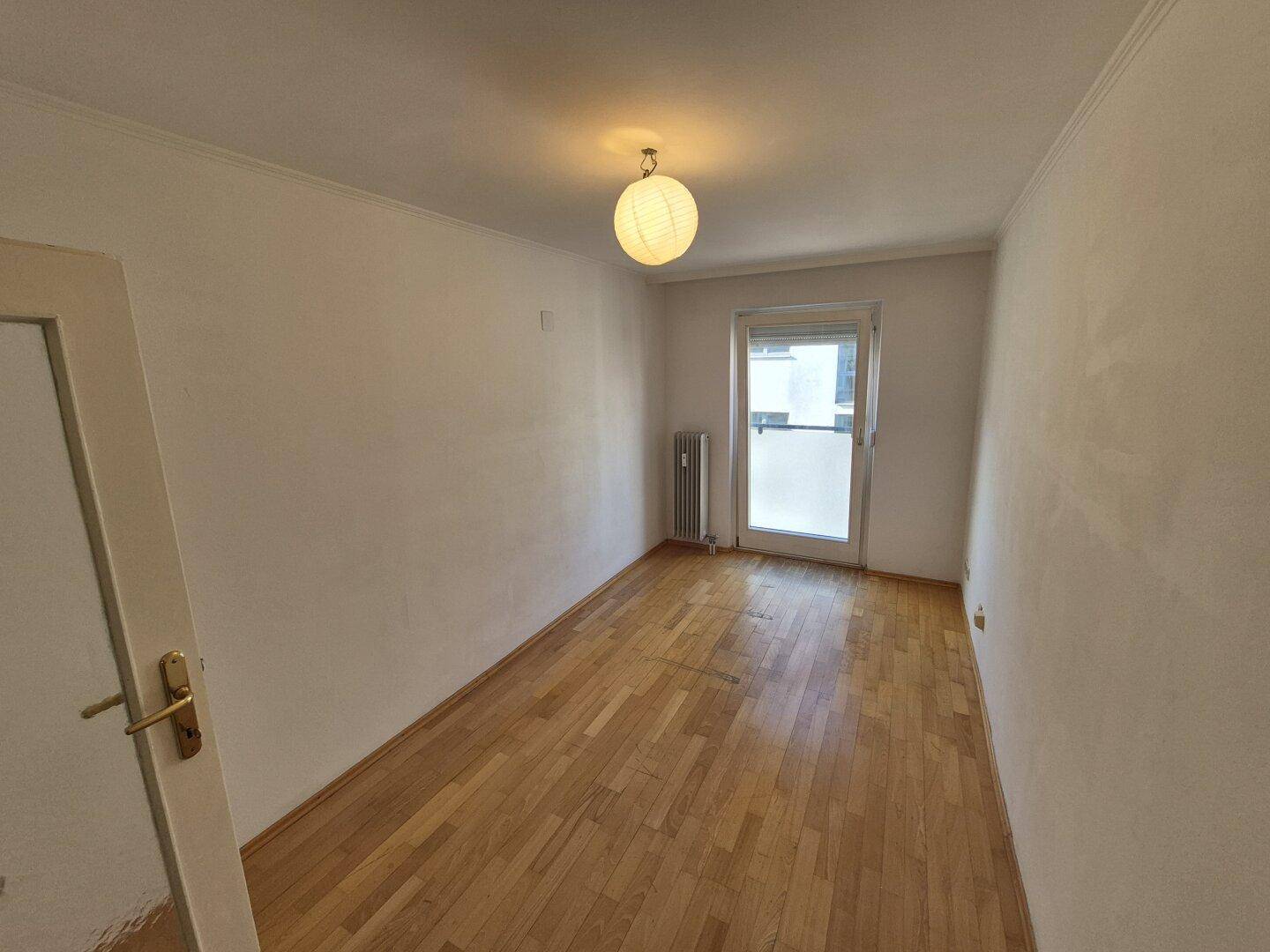 Helles Schlafzimmer mit Parkettboden und Fenster, das viel natürliches Licht hereinlässt.